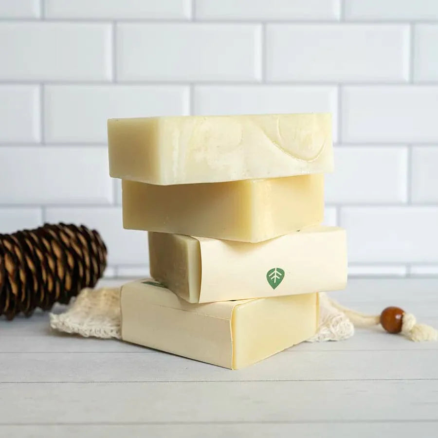 Stack of natural soap bars with a leaf logo on a white surface and tiled wall background