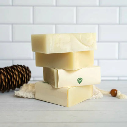 Stack of natural soap bars with a leaf logo on a white surface and tiled wall background