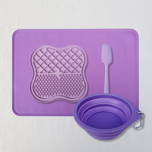 Purple silicone mat with textured design, a small spatula, and a collapsible bowl on a light gray background.